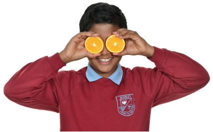 school boy holding up orange slices in front of their face and pretending that that they are eyes!